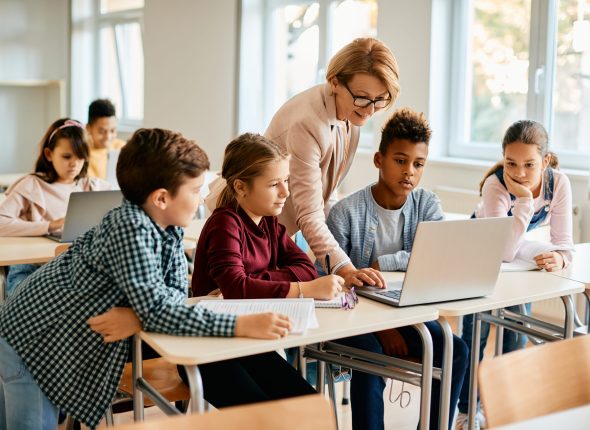 Group of elementary students having computer class with their teacher in the classroom.